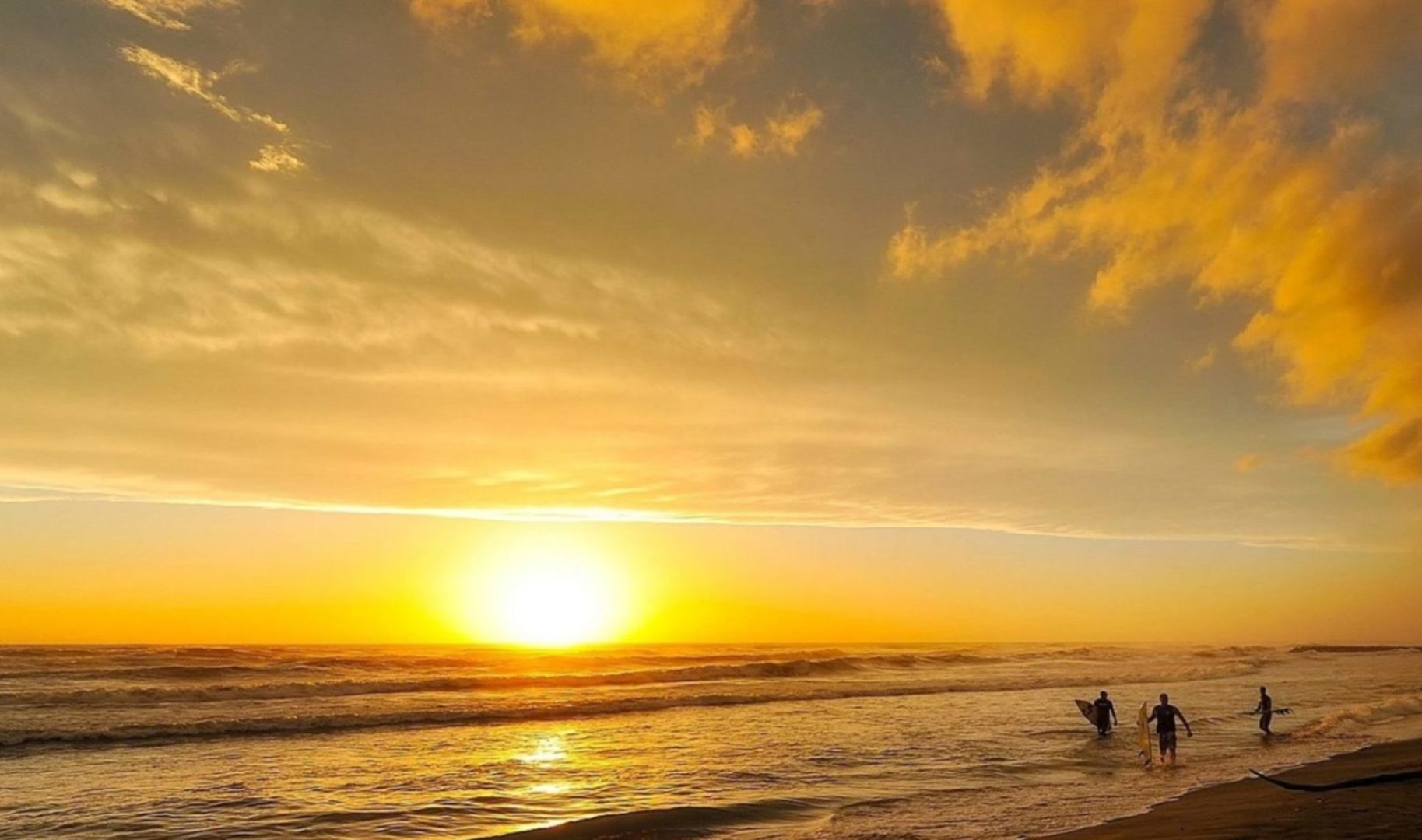 Alcançar a Liberdade Financeira representada pela imagem do mar dourado pelo pôr do sol com céu dourado ouro e três surfistas